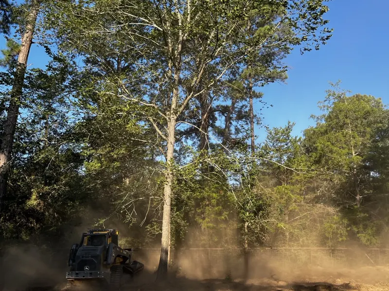 Track loader and mulcher working dusty ground under kept trees on a retreat property